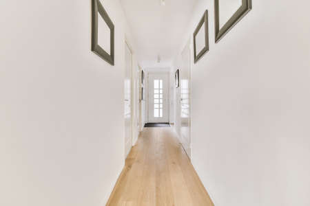 Light narrow hallway with many doors in white walls and glowing lamp over lumber floorの写真素材
