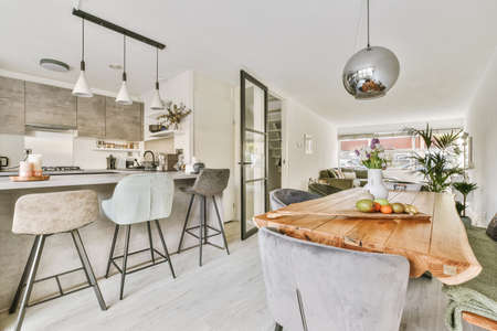 Wooden table with vase of flowers under black pendant lamp in modern living room near window
