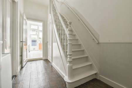 Light hallway with entrance door in two level apartment with minimalist wooden staircase leading...