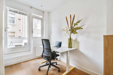 A bright white work area with a small laptop and an ergonomic chair in a cozy house