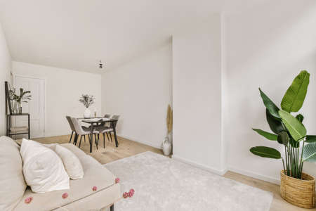 Shabby wooden table with chairs and vase located near comfortable couch against light walls with...