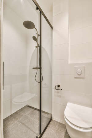 Shower faucets attached to tiled wall near glass partition and ornamental curtail in washroom at homeの写真素材