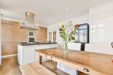 Wooden table and comfortable chairs placed near kitchen furniture in modern light flat