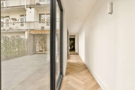 Room with door to balcony and narrow long corridor in perspective in modern house with ceiling beams