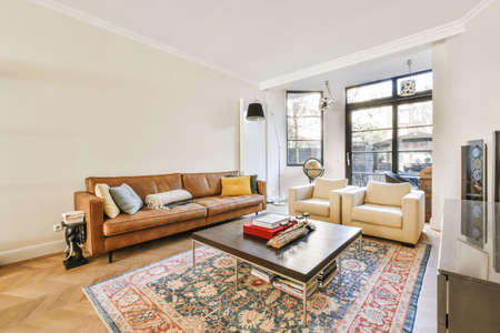Comfortable sofa with soft cushions located under stylish chandelier in spacious light living room...
