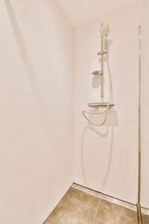 Shower faucets attached to tiled wall near glass partition and ornamental curtail in washroom at...
