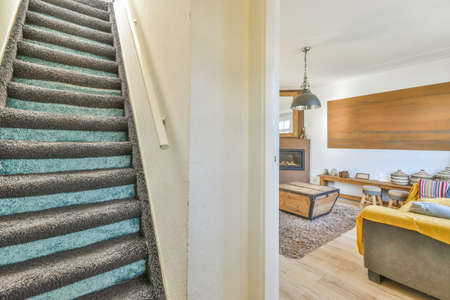 A spacious bright corridor with a wooden staircase and an entrance to the dining room with a window