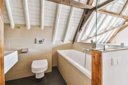 Modern flush toilet and ceramic sink installed on white tiled walls near mirror and towel in small...
