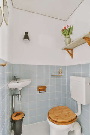 Modern flush toilet and ceramic sink mounted on blue tiled walls in a small lavatory at home with wood elementsの写真素材