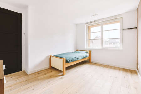 Comfortable bed without ornamental blanket, near window and wardrobe in light bedroom