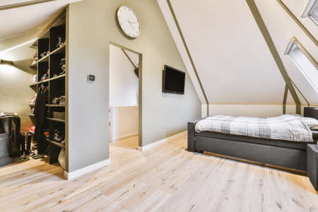 Comfortable bed placed near white wall in modern minimalist style mansard bedroom with windows and...
