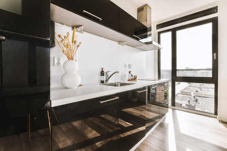 Fragment of interior of light narrow home kitchen with minimalist style white furniture with sink...