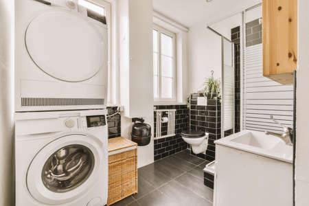 Shower and bathtub in a black and white bathroom with a washing machine and a wooden cabinet with a...