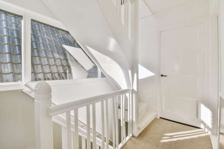 Closed white door of room located near framed pictures and stylish lamp on top of stairway at home