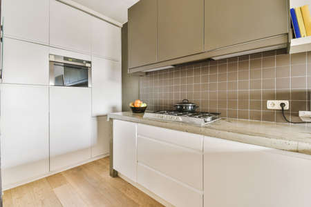 Fragment of interior of light narrow home kitchen with minimalist style white furniture with sink...