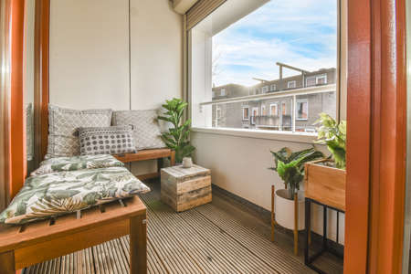 Narrow brick balcony with metal railings, wooden chair and door with glass leads to the kitchen