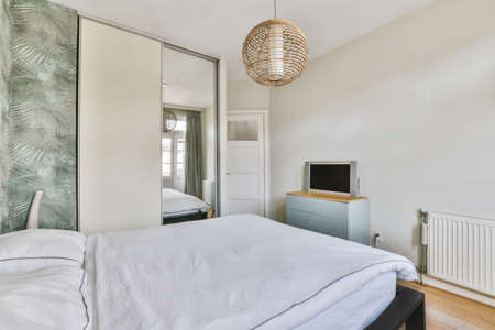 A comfortable bed with a blanket sits against a wall with green prints and next to a wardrobe with a...