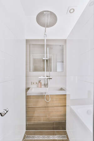Shower faucet hanging on white tiled wall in light washroom in modern flat