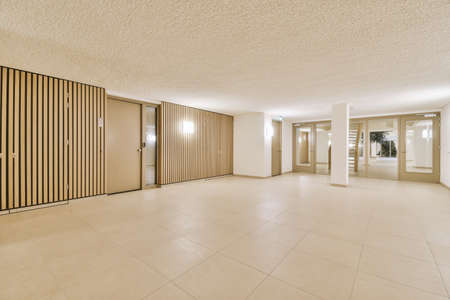 Light hallway with entrance door in two level apartment with minimalist wooden staircase leading...