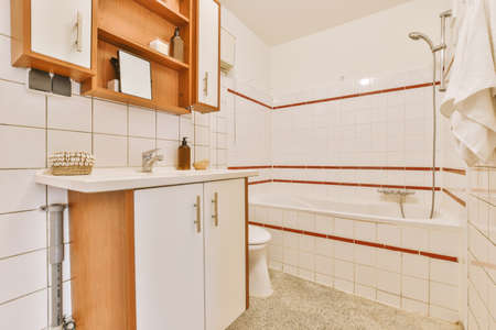 Interior of modern bathroom with bathtub and sink in wooden counter furnished with wooden shelf rack
