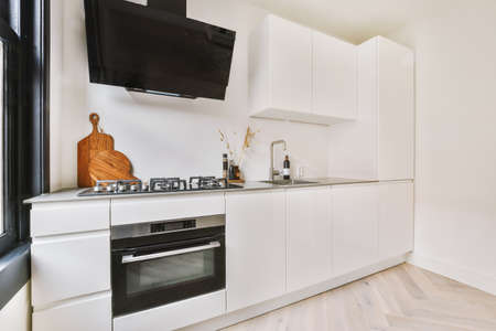 Well organized small home kitchen interior with sink under window and light furniture with stove and...