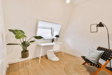 Comfortable chair placed near table in mansard light home office in contemporary flat