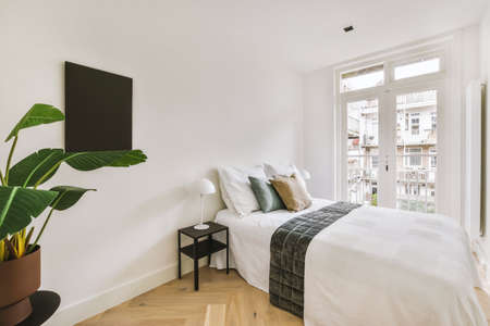 Home interior design of bedroom with bed and wooden wardrobe placed in corner near window in modern apartmentの写真素材