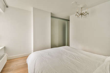 Home interior design of bedroom with bed and wooden wardrobe placed in corner near window in modern apartmentの写真素材