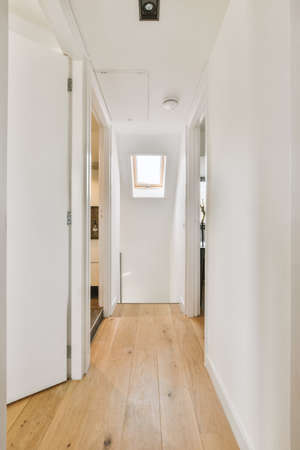 Retro cabinet with decorations and mirror located near stairway and door into living room in corridor of houseの写真素材