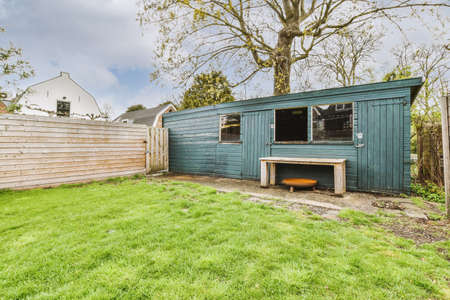 Wooden blue barn with a bench near a wooden fence in the courtyard of a modern house