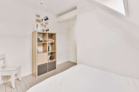 Comfortable bed placed near green wall in modern minimalist style mansard bedroom with windows