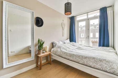 Home interior design of bedroom with bed and wooden wardrobe placed in corner near window in modern...
