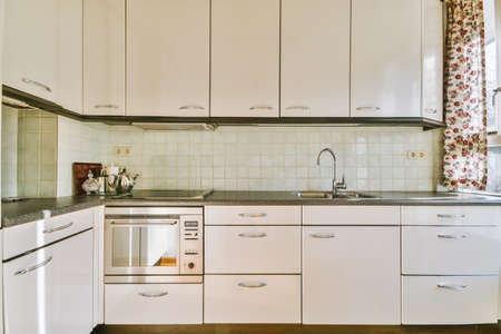 Modern interior design of a corner home kitchen with white cabinets and wooden floor in a modern...