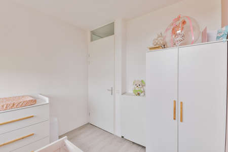 Interior of white room with baby crib and armchair near window with blue chest of drawers in daylightの写真素材