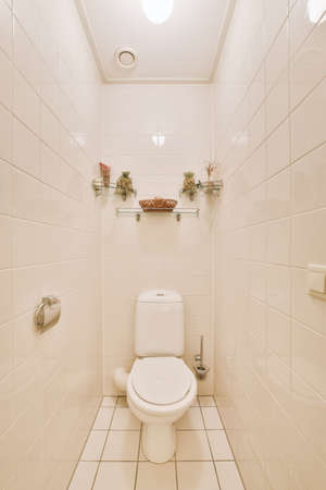 Wall hung toilet and small sink in corner in lavatory room with beige tile