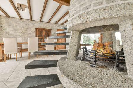 Stylish luxury home interior design of cozy living room with burning fireplace and comfy sofa and carpet in daylightの写真素材