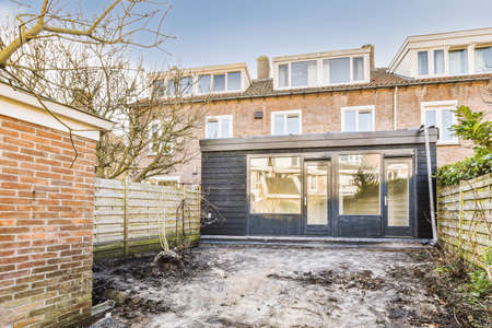 Untidy courtyard with wooden fence, garbage cans and clay brick house