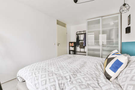 Modern home interior design of small mansard bedroom with white walls and soft cozy bed and...