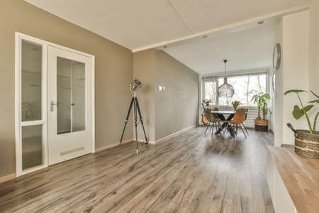 Simple interior of light living room with gray sofa in front of TV and dining table against window