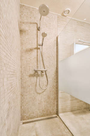 Shower faucets attached to tiled wall near glass partition and ornamental curtail in washroom at...