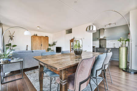 Table with chairs and flowers located near lounge area and kitchen in spacious room of contemporary...