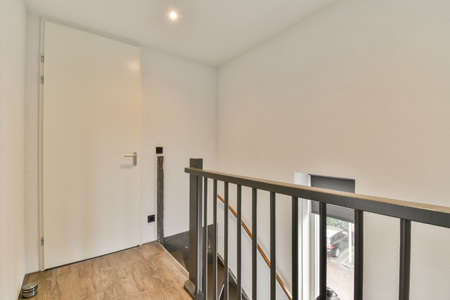 Closed white door of room located near framed pictures and stylish lamp on top of stairway at home