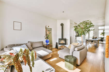 Large corner sofa with soft cushions, near the fireplace in a bright living room with potted plants,...