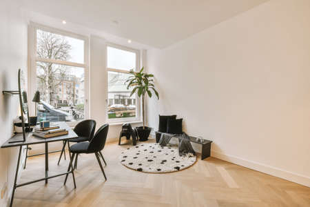 A table with a round mirror, with a lamp and chairs, is located against a white wall opposite a...