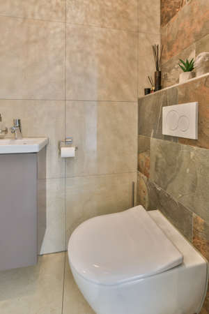 Flush toilet located between sink and shower in small tiled bathroom of contemporary apartment
