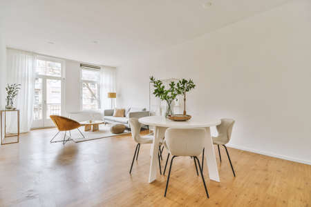 Stylish home interior design of spacious living room with large windows and white walls furnished...