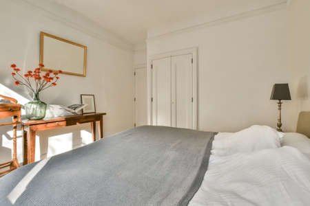 Modern home interior design of small mansard bedroom with white walls and soft cozy bed and minimalist style shelves in daylight with illuminationの写真素材