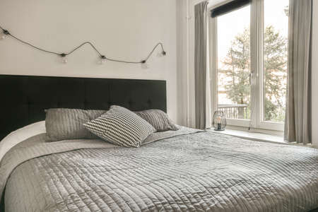 A spacious bright bedroom with a minimalistic black wardrobe and a large panoramic window