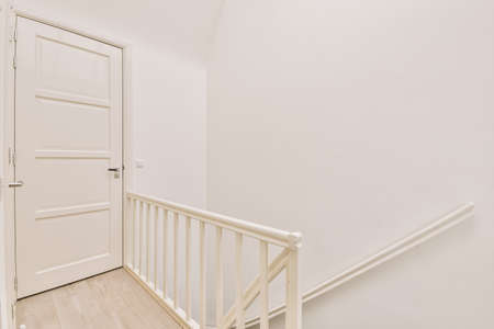 Closed white door of room located near framed pictures and stylish lamp on top of stairway at home