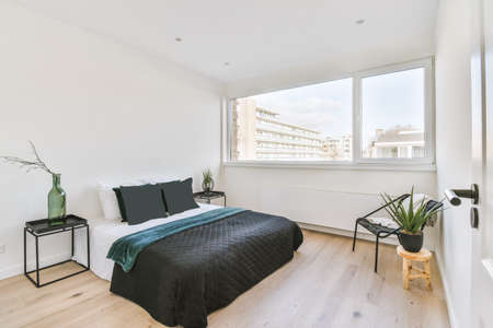 Spacious bright bedroom with white walls and wooden floor by the window